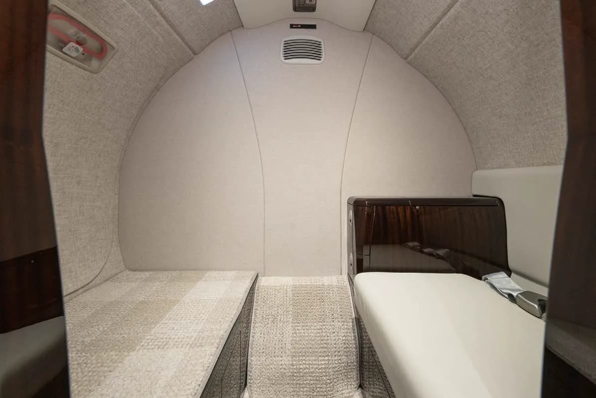 The aft section of a private jet cabin, showing a comfortable divan and a dark wood cabinet.