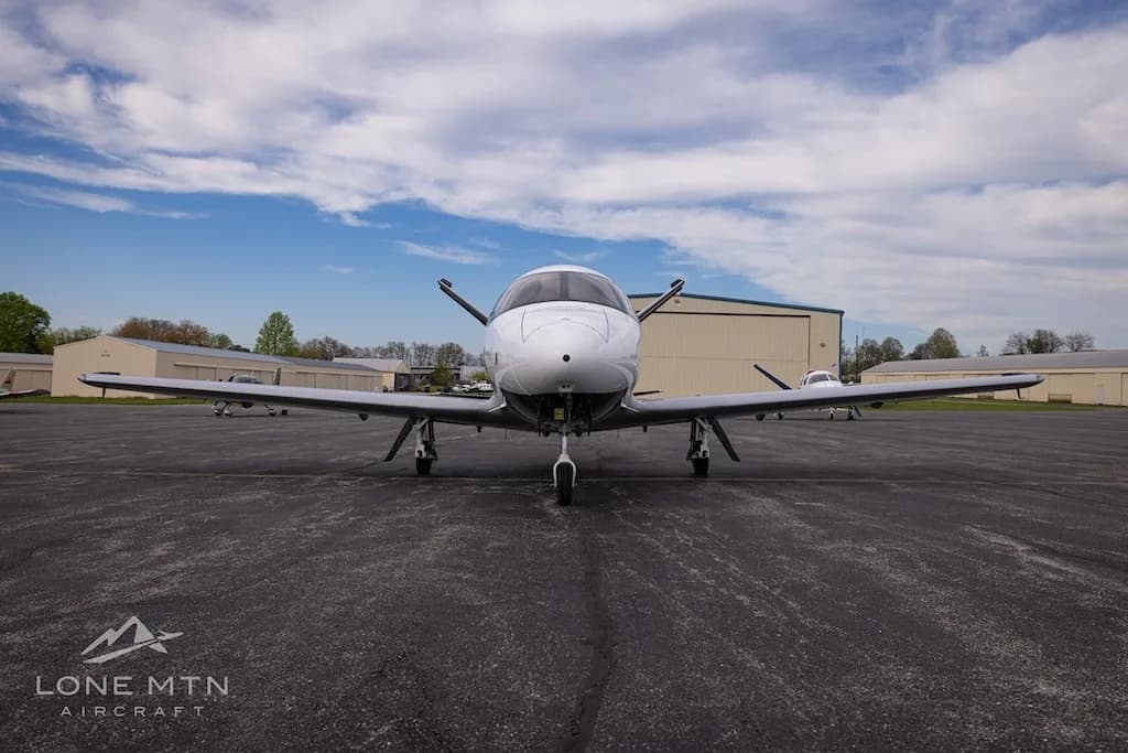 A front view of a white Cirrus Vision Jet (N63KL) parked on an asphalt apron with hangars in the background.