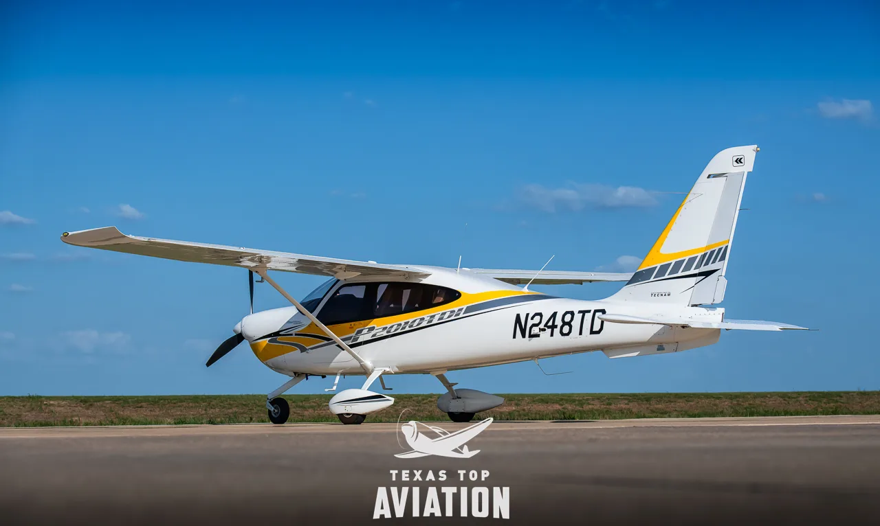 A white and yellow Tecnam P2010 TDI aircraft (N248TG) parked on an airfield under a blue sky.