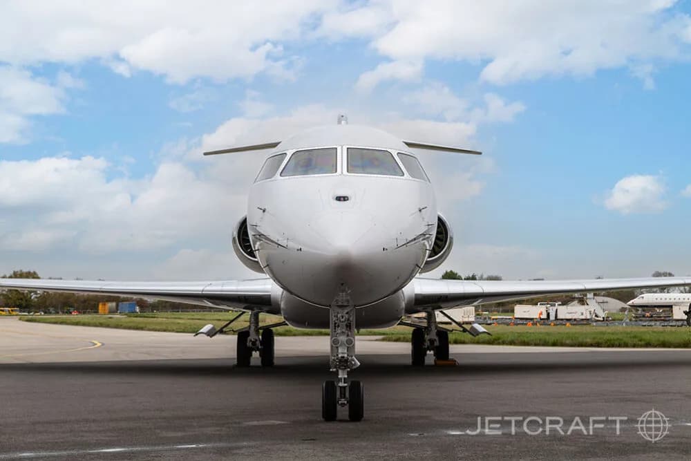 A head-on view of a white Bombardier Global business jet with its landing gear extended on an airfield.