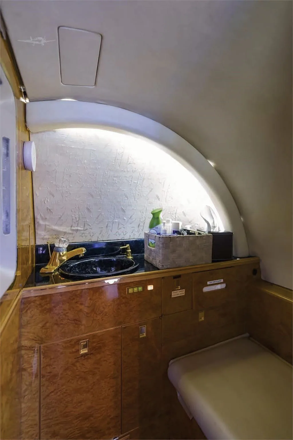 The aircraft's lavatory features a black sink with a gold faucet, wood cabinetry, and a light-colored vanity area.