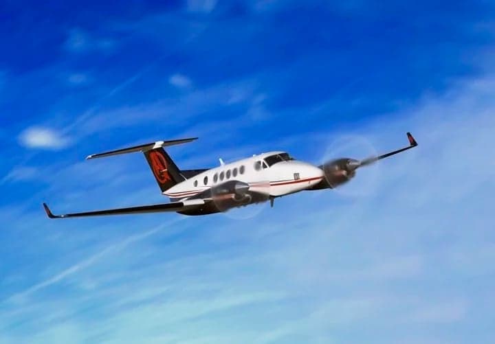 A King Air aircraft with a custom black, white, and red paint scheme in flight against a blue sky.