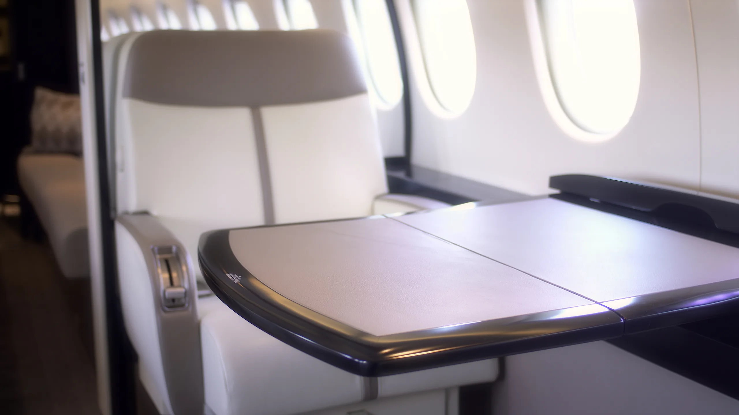 A close-up of a fold-out table next to a light-colored cabin seat in a business jet.