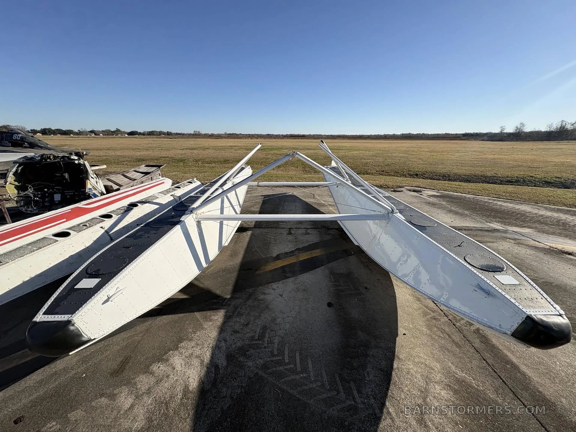 Two white aircraft floats with black tops are seen from the front on an airfield tarmac.