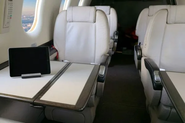The aircraft's interior cabin with light-colored seats and a tablet resting on a fold-out table.