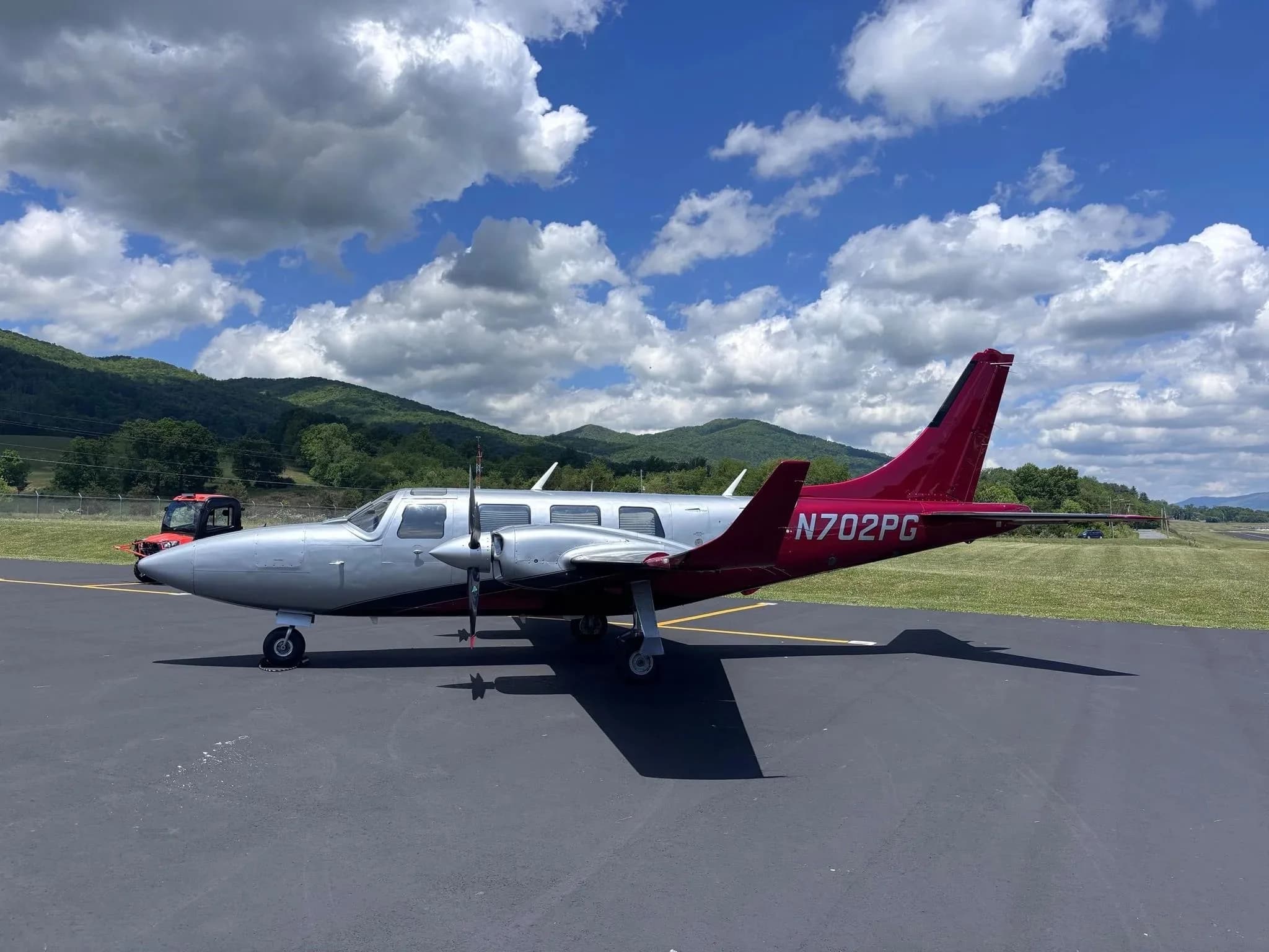 A side view of a silver and red twin-engine Aerostar aircraft (N702PG) on an airfield.