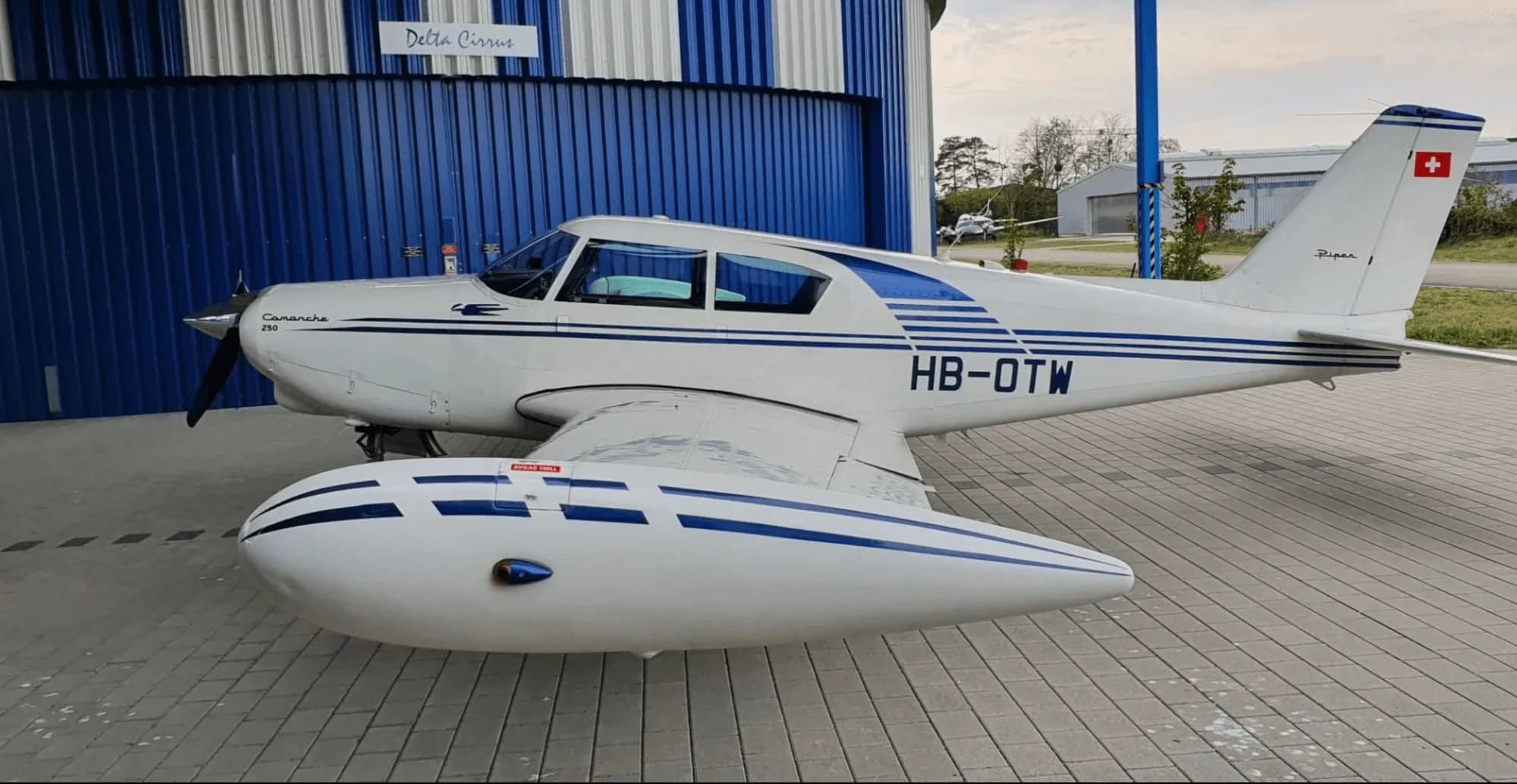A Piper Comanche 250 parked in front of a hangar.