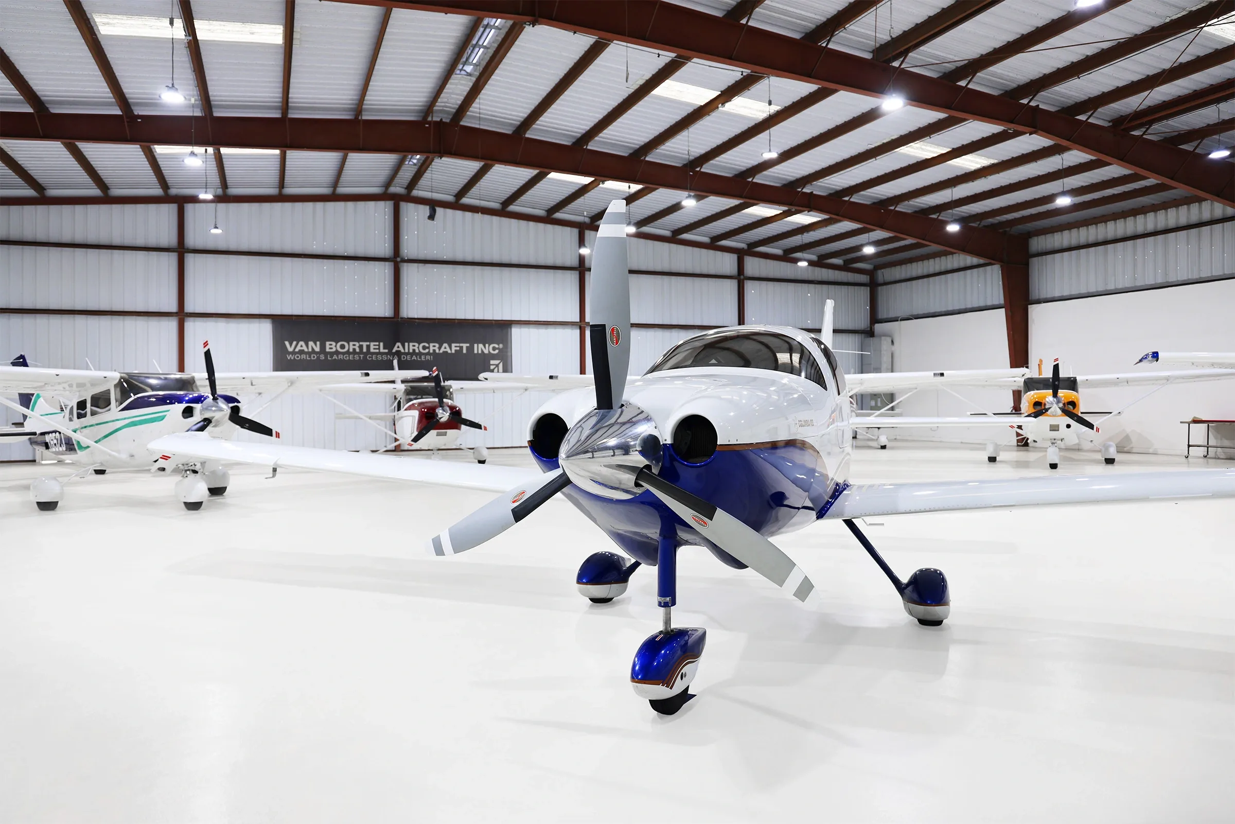 A white and blue Columbia 400 aircraft with registration N918LV is parked in a hangar, viewed from the front.