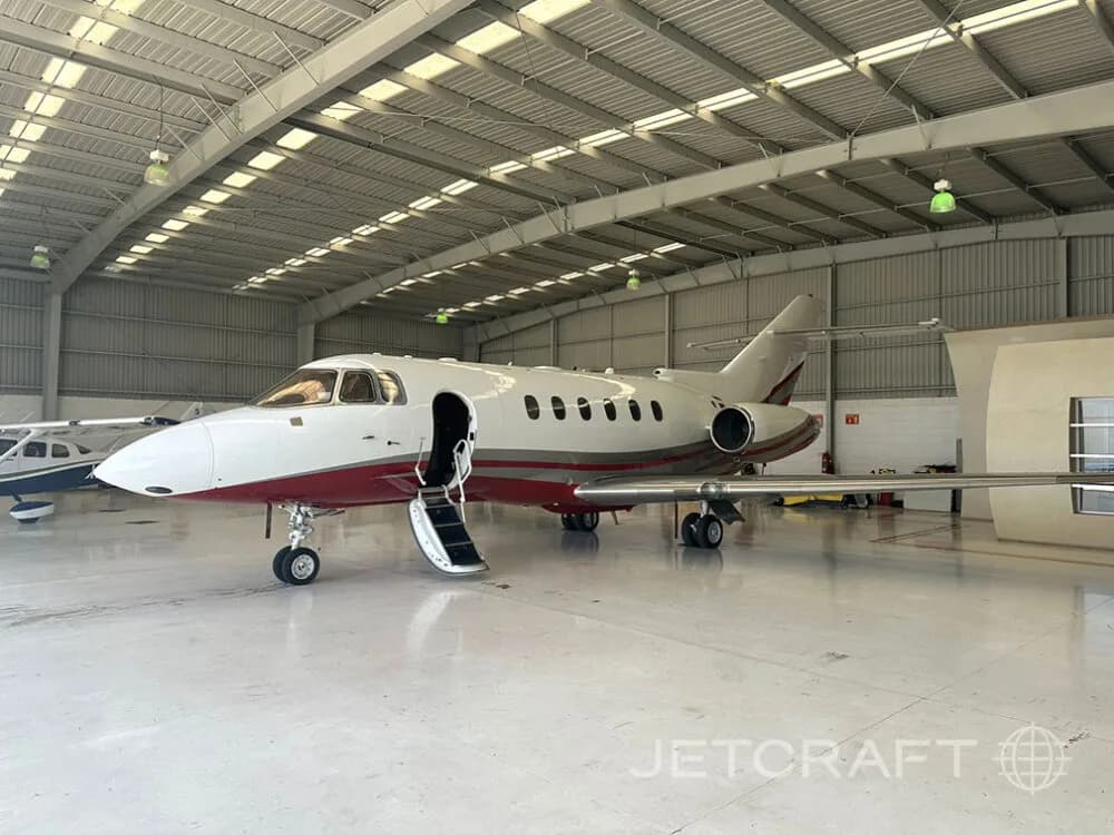 A white and red business jet with its main door open and stairs extended, parked inside a hangar.