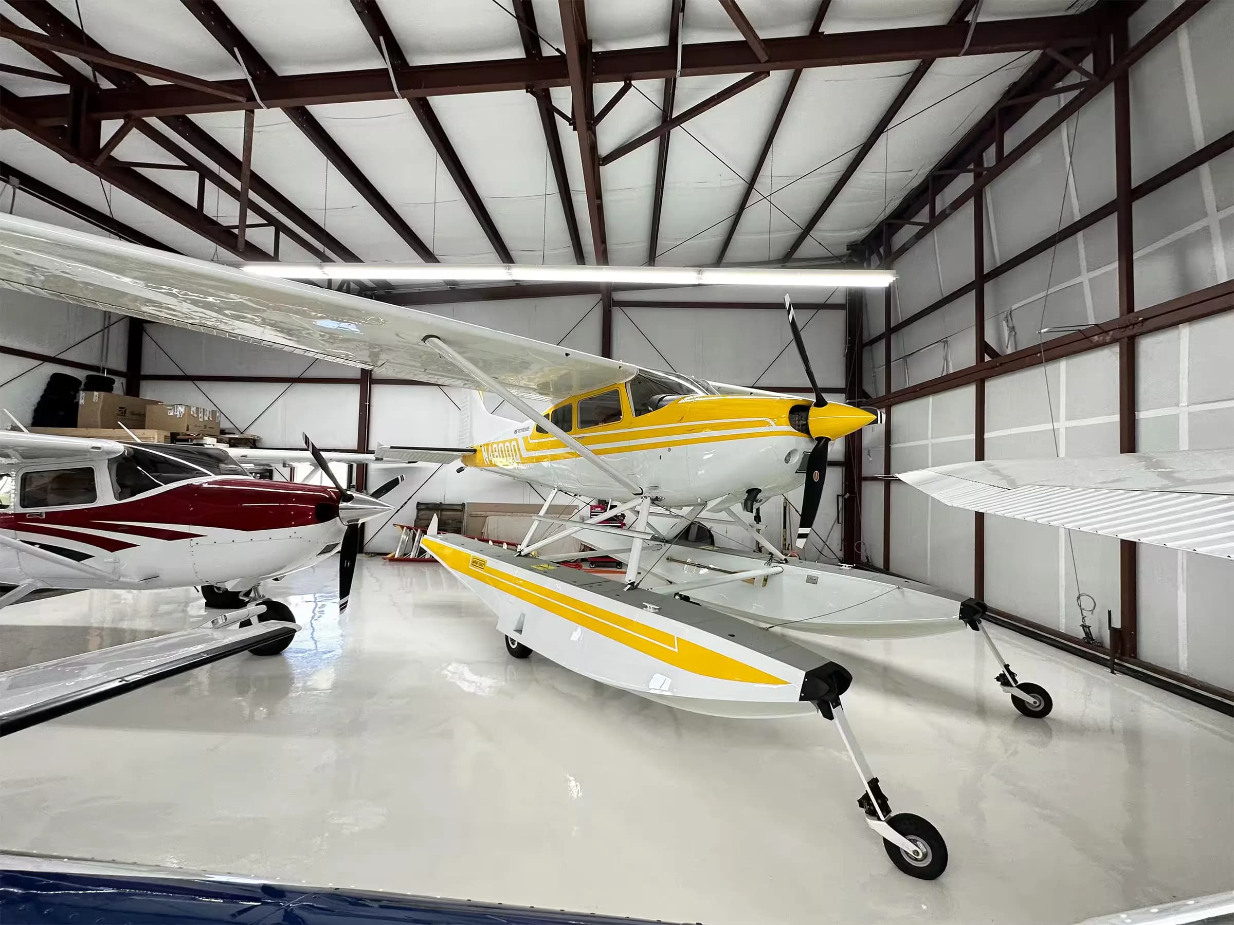 A yellow and white Cessna 185 floatplane, N4800Q, parked inside a hangar next to other aircraft.