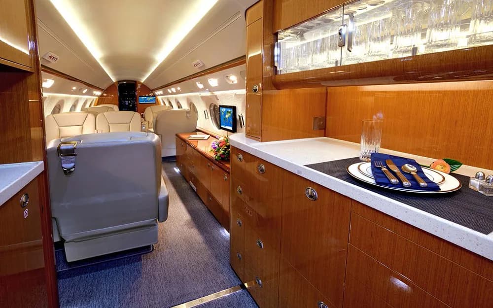 The aircraft's galley area with a white countertop, wooden cabinetry, and a set plate, looking into the main cabin.