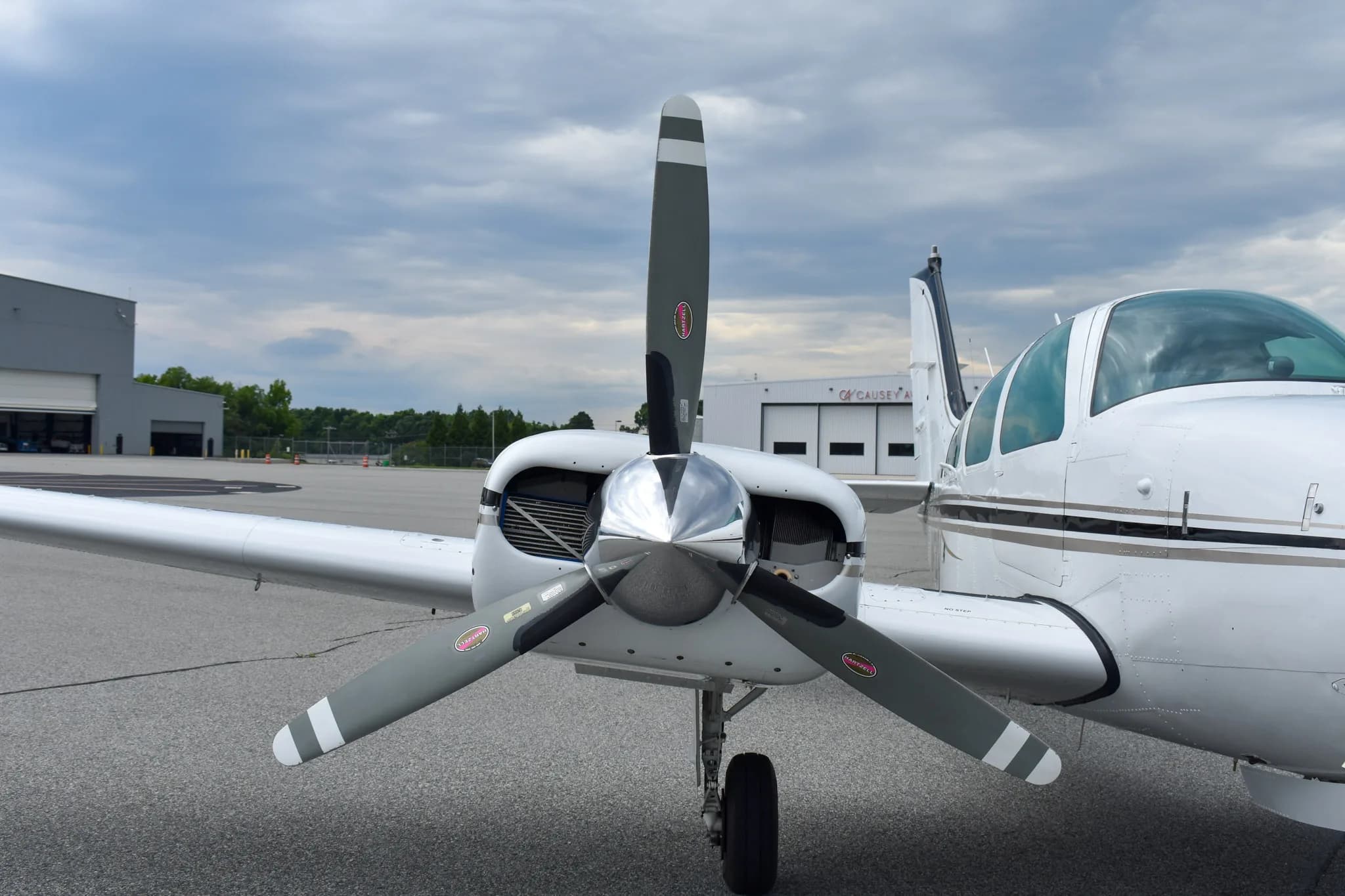 A front view of the left engine and propeller of a white Beechcraft Baron aircraft on an airfield.