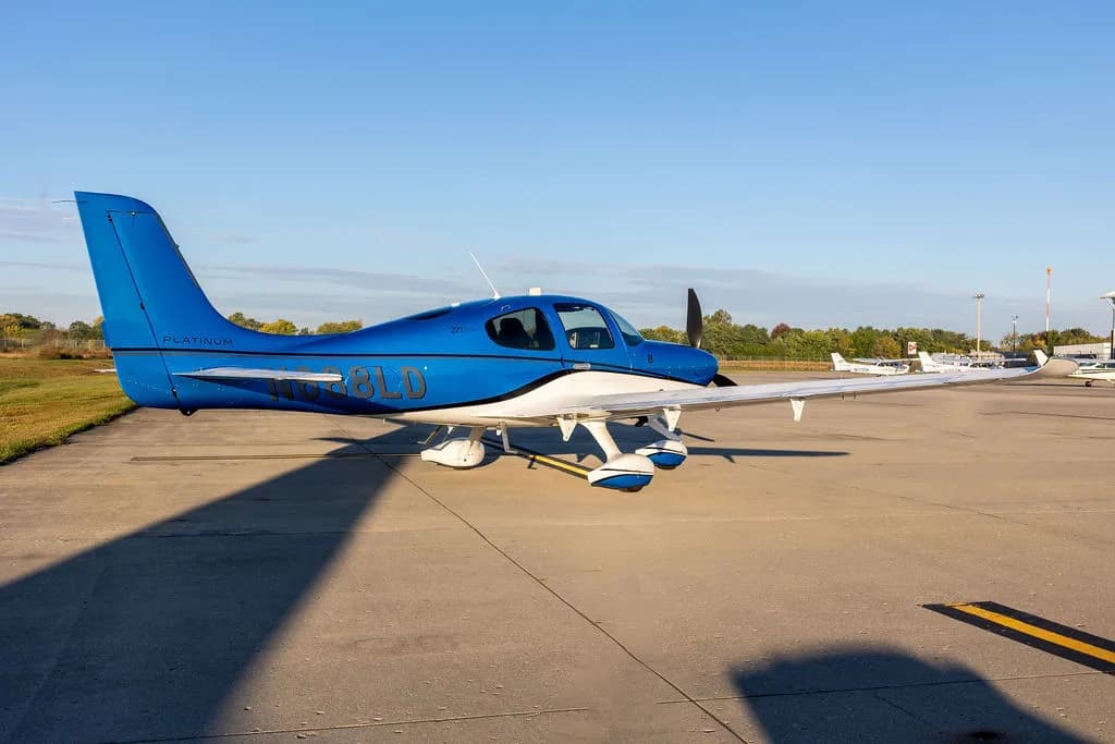 A blue and white Cirrus SR22 aircraft with registration N688LD parked on an airfield with other aircraft in the distance.