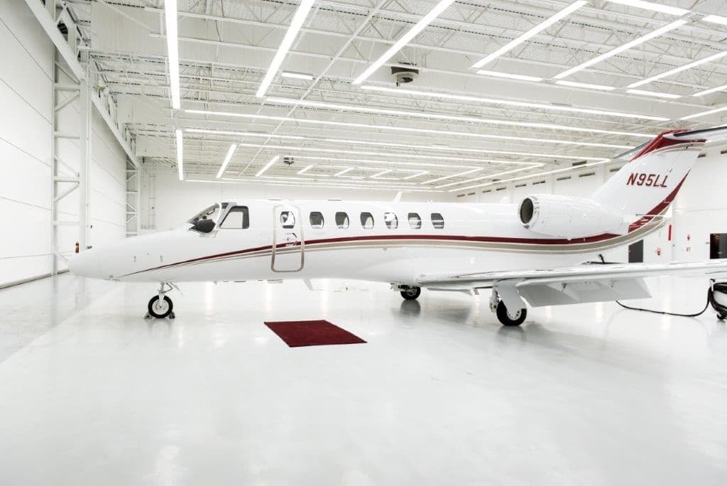 A white business jet with red and grey stripes, tail number N95LL, parked in a brightly lit hangar.