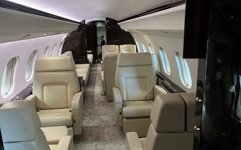 A long view down the private jet cabin, showing multiple cream-colored individual seats and dark wood paneling.