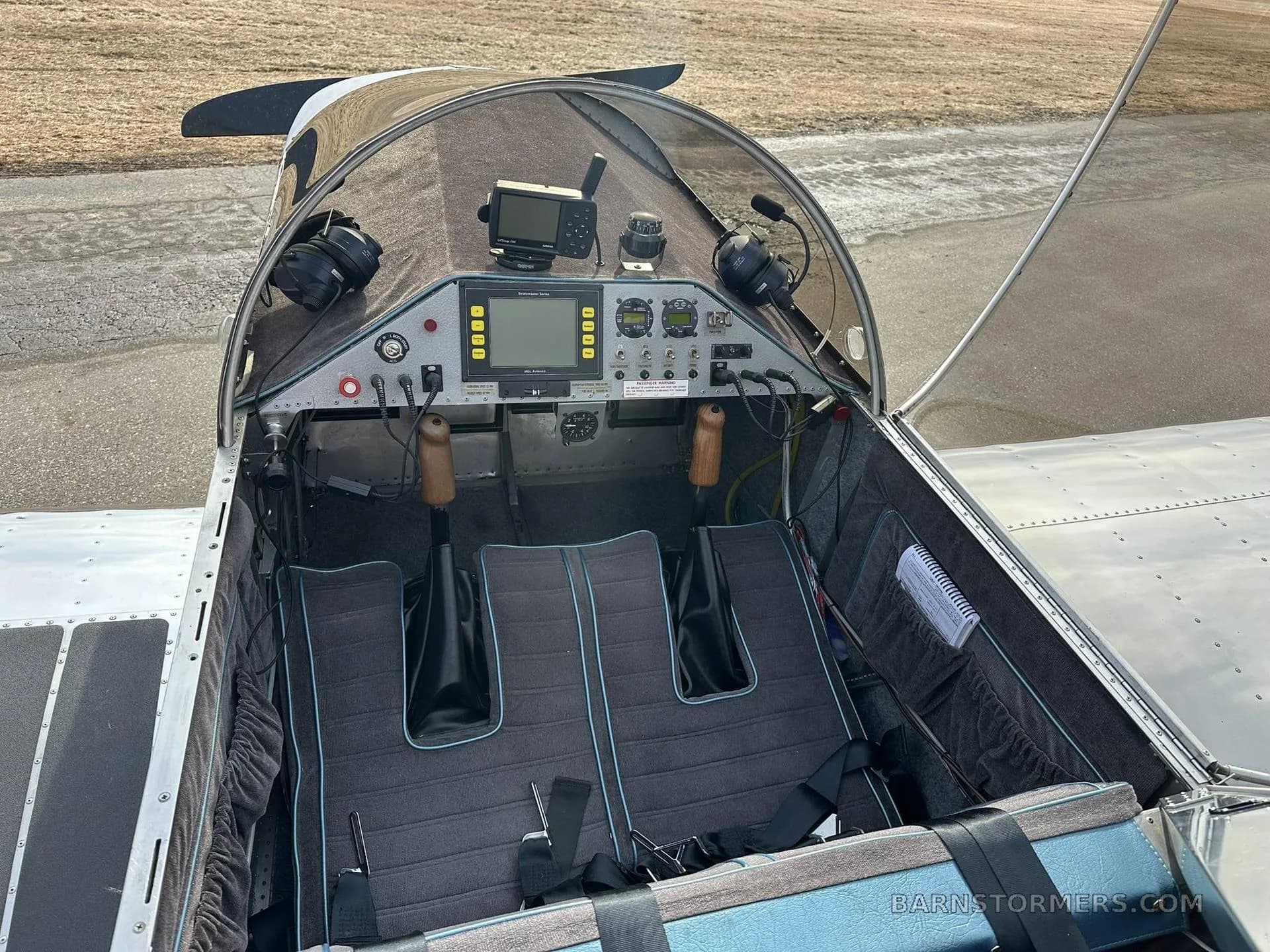 The cockpit of an experimental aircraft, showing the instrument panel with screens, dual controls, and two seats with blue trim.