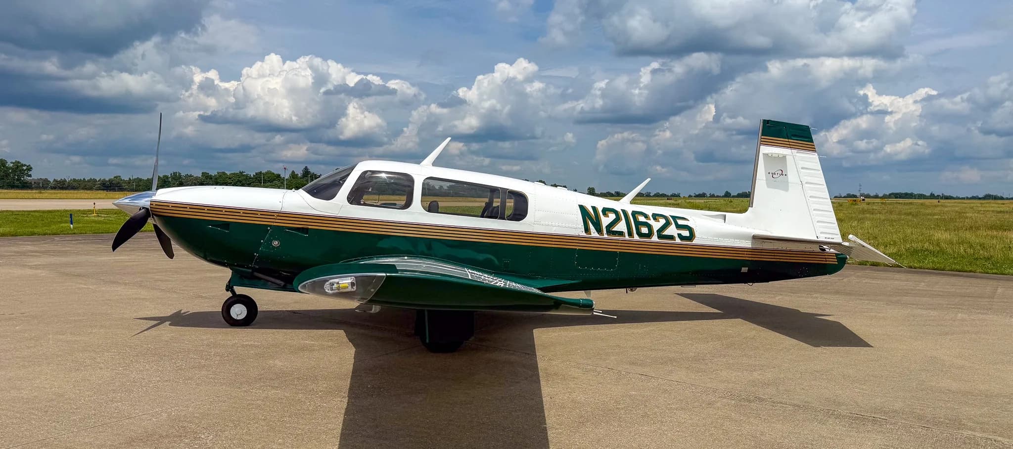 A side view of the white and green Mooney M20 aircraft with registration N21625 on an airfield.