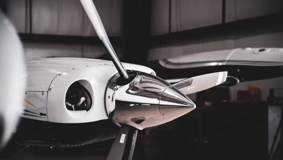 Close up of a propeller and cowling of a white aircraft in a hangar.