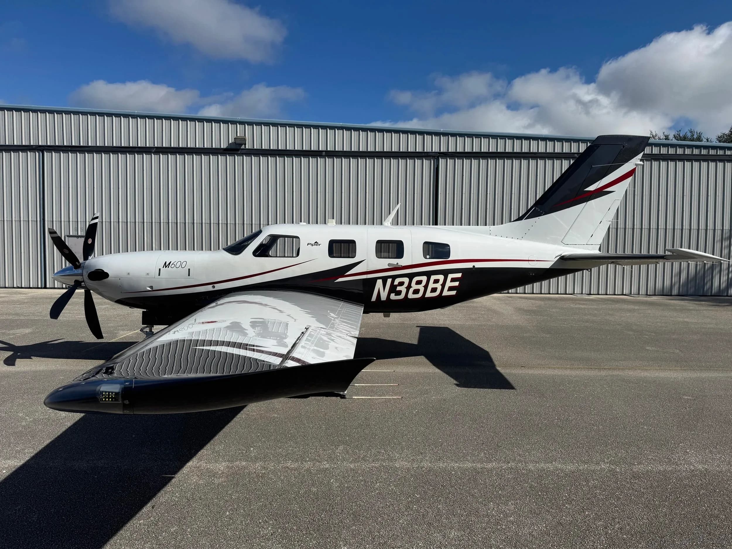 A Piper M600 with a white and black paint scheme is parked in front of a hangar.