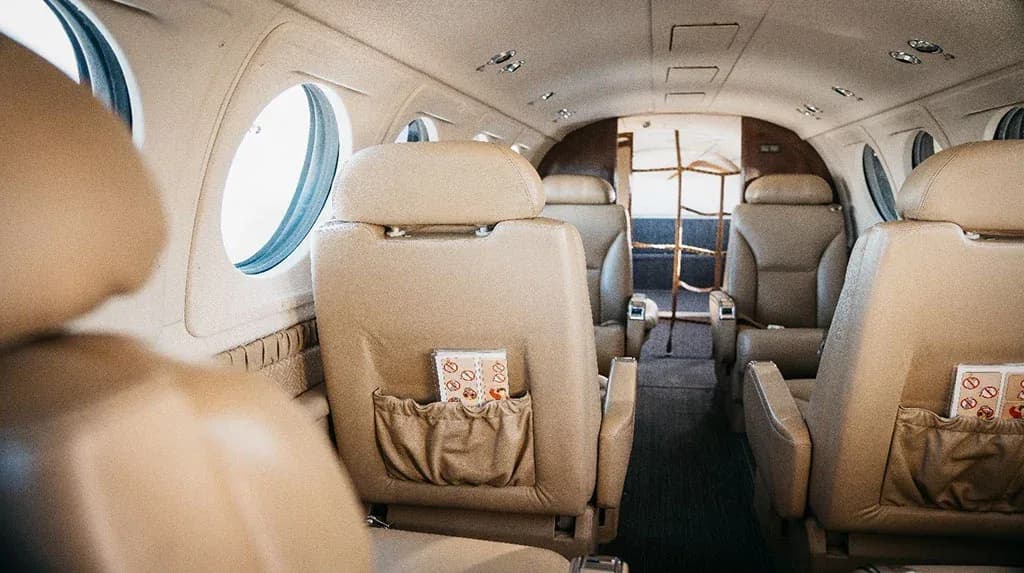 View of the aircraft cabin with multiple rows of tan leather seats and windows.