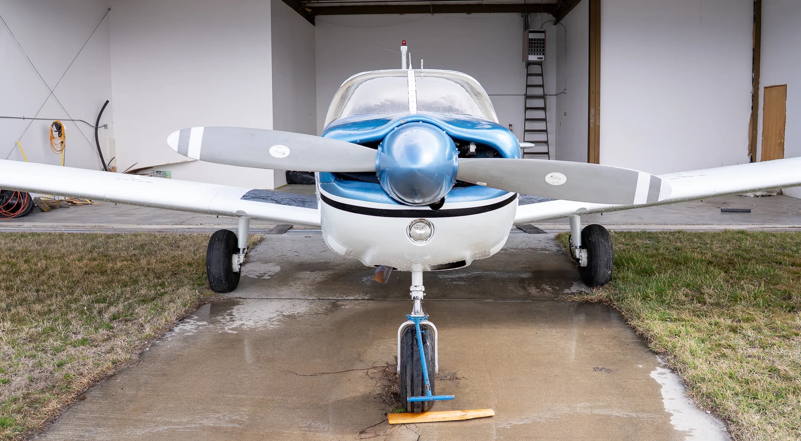 Front view of a white and blue single-engine propeller aircraft parked in a hangar.