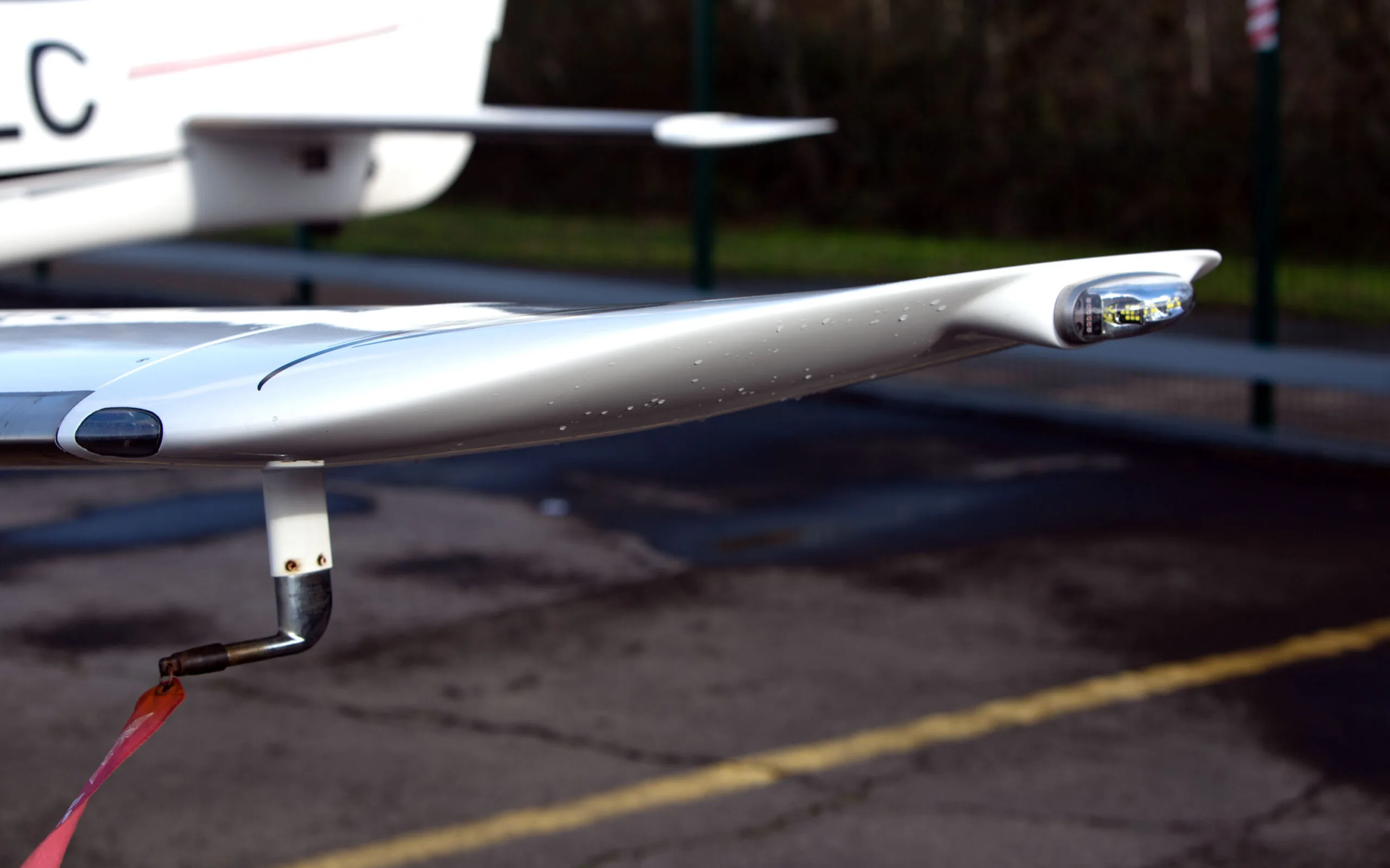 A close-up view of the white wingtip of a Cirrus SR22 G3 aircraft, showing the navigation light and a red pitot tube cover.