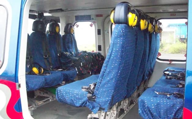 The interior of a helicopter cabin showing rows of blue patterned seats with yellow headsets.