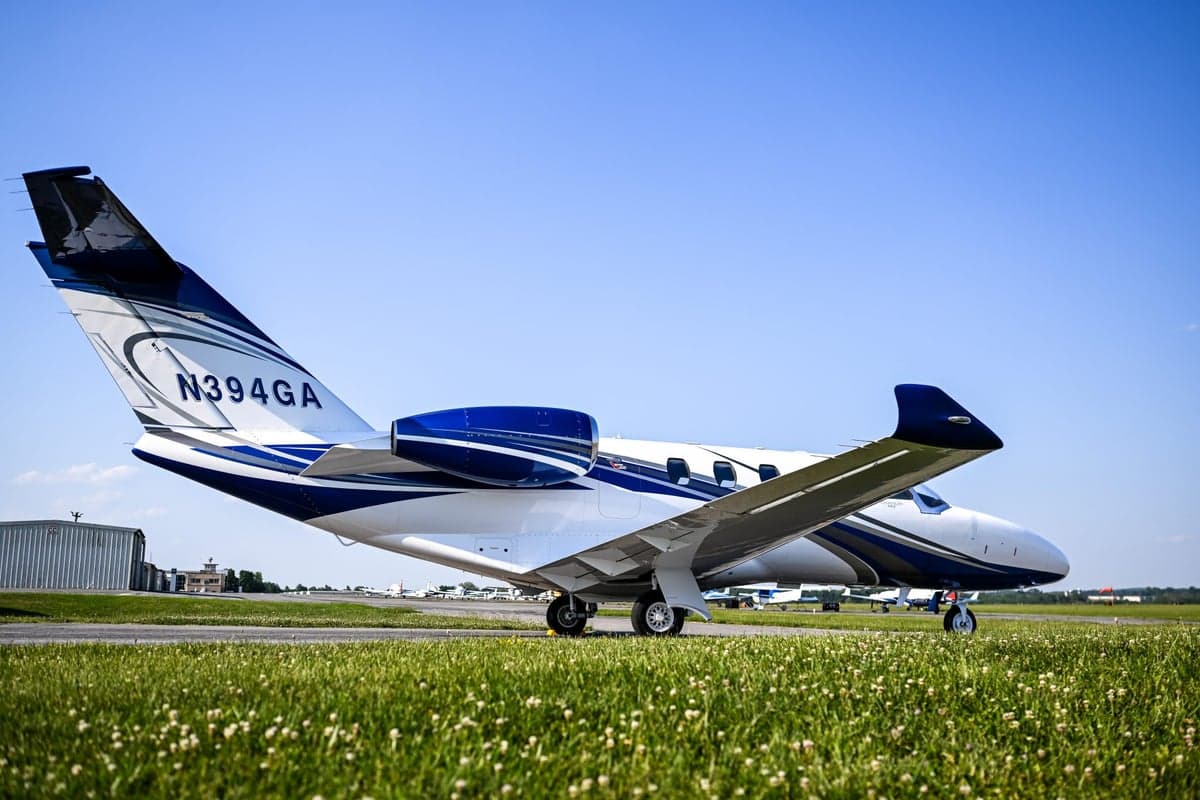 Side view of a white and blue Cessna Citation M2 jet, registration N394GA, parked on an airport tarmac.