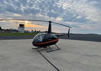 Robinson R44 Raven II helicopter on the tarmac at sunset.