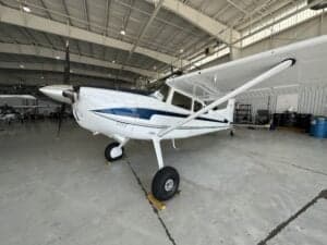 A Cessna aircraft with a white and blue paint scheme is parked in a hangar.