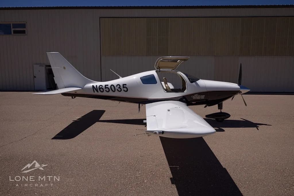 A white and black single-engine aircraft, N65035, with its gull-wing doors open, parked in front of a hangar.