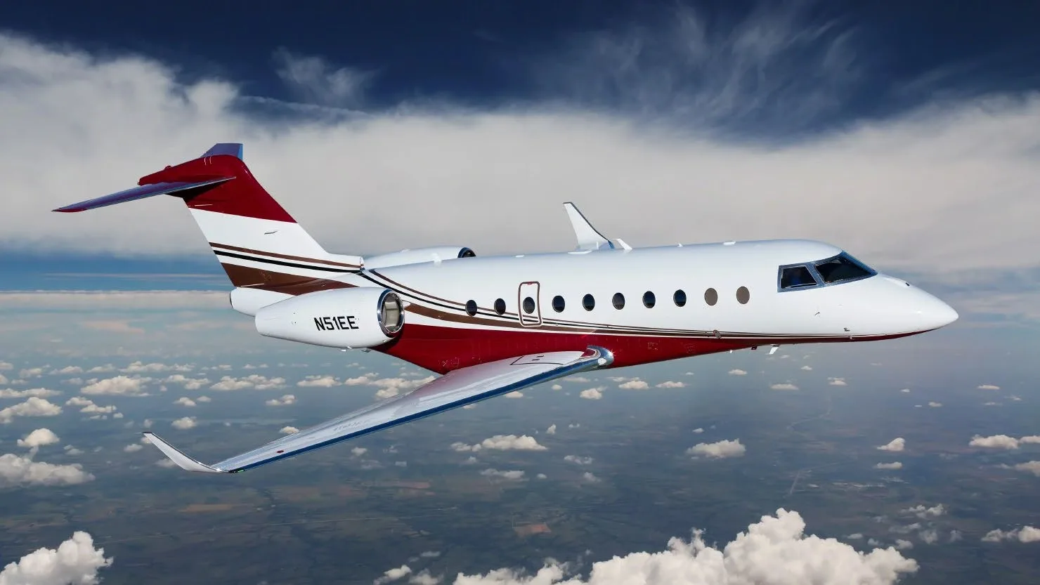 A white and red business jet with registration N51EE flies through a cloudy blue sky.