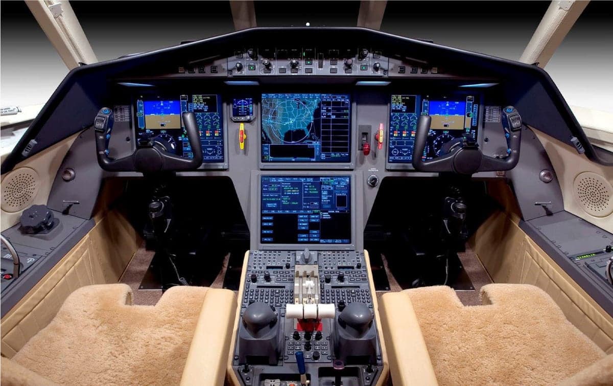 A modern aircraft cockpit with multiple large digital displays and two control yokes.