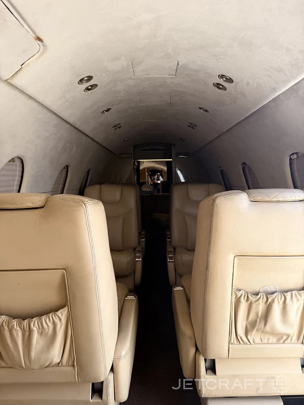The interior cabin of a private jet with tan leather seats, looking towards the rear of the aircraft.