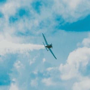 An aircraft flies through the sky, leaving a smoke trail.