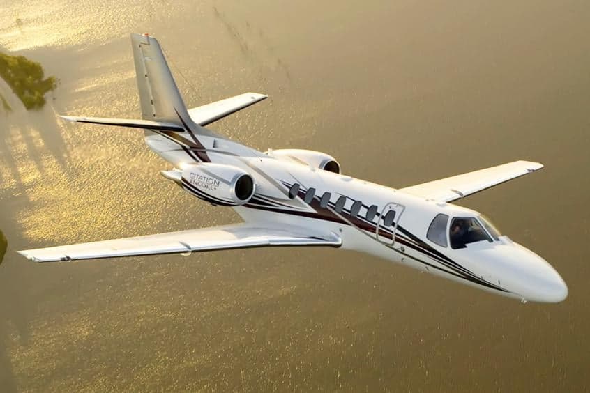 A Citation Encore+ in flight over water.