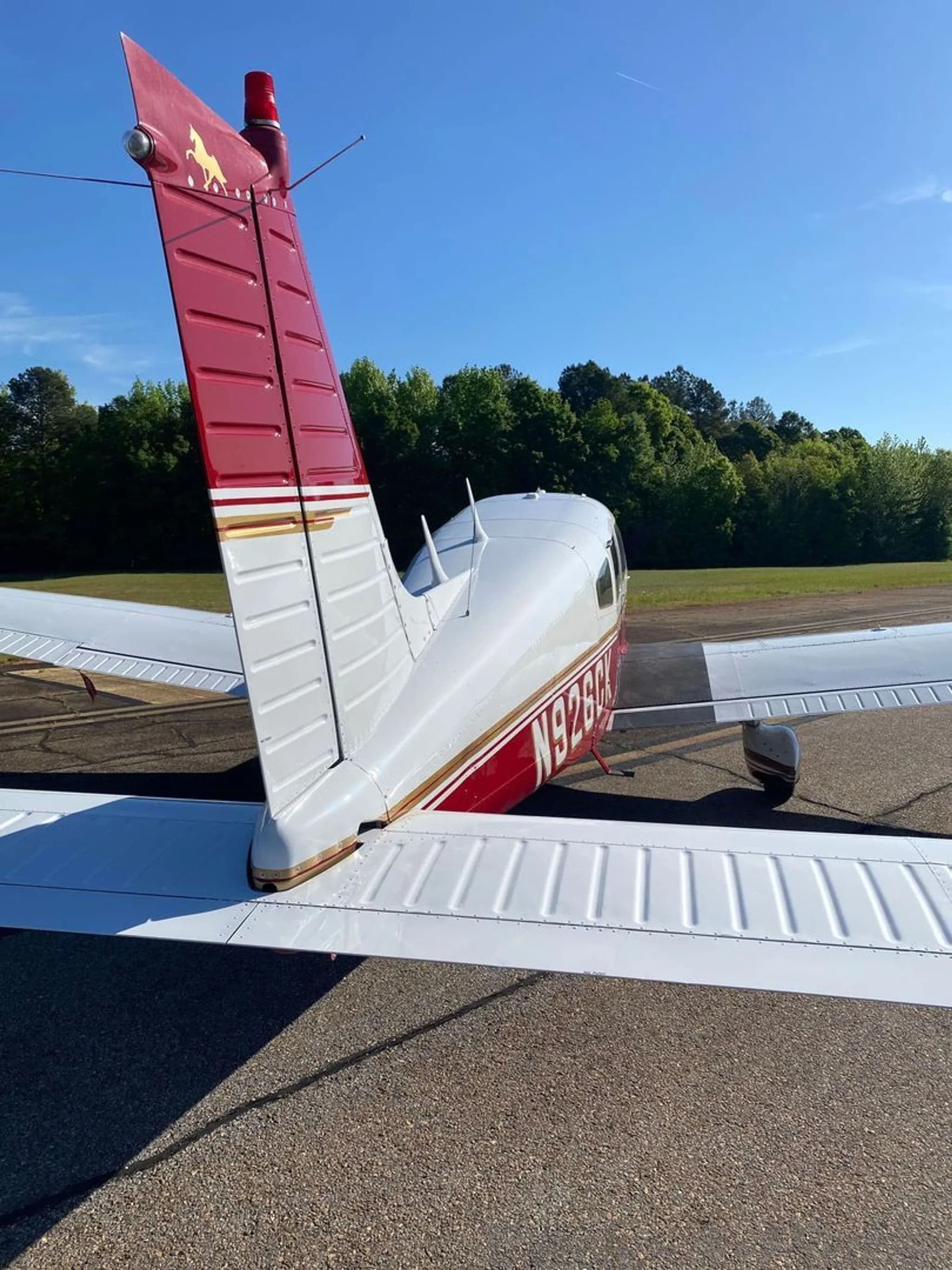 A rear view of the white and red Piper Arrow II (N926CK) showing the tail with a golden horse logo and right wing.