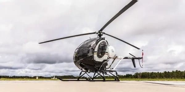 A black and white MD 500 helicopter is parked on the tarmac.