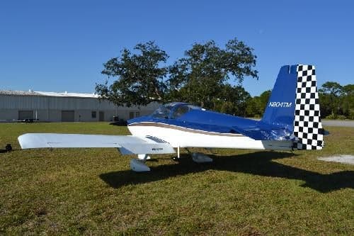 A blue and white aircraft with a checkered tail is parked on a grassy field near a building.
