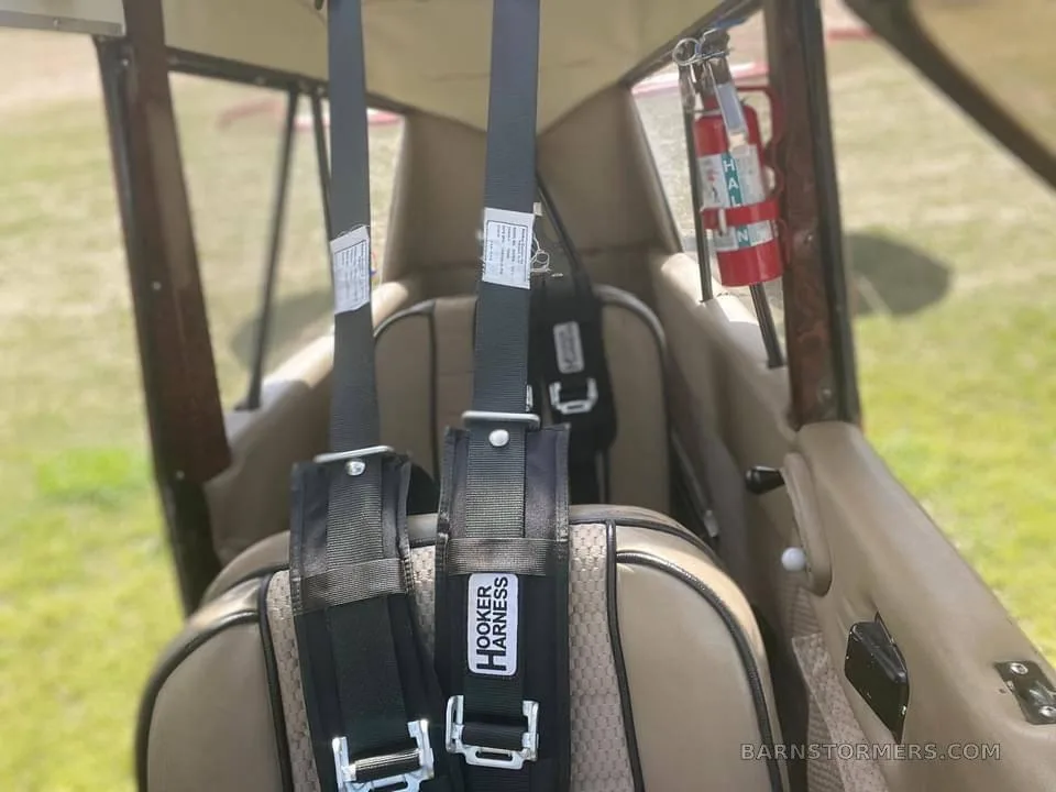 The tan interior cabin of a small aircraft, showing two seats with "Hooker Harness" seatbelts and a fire extinguisher.