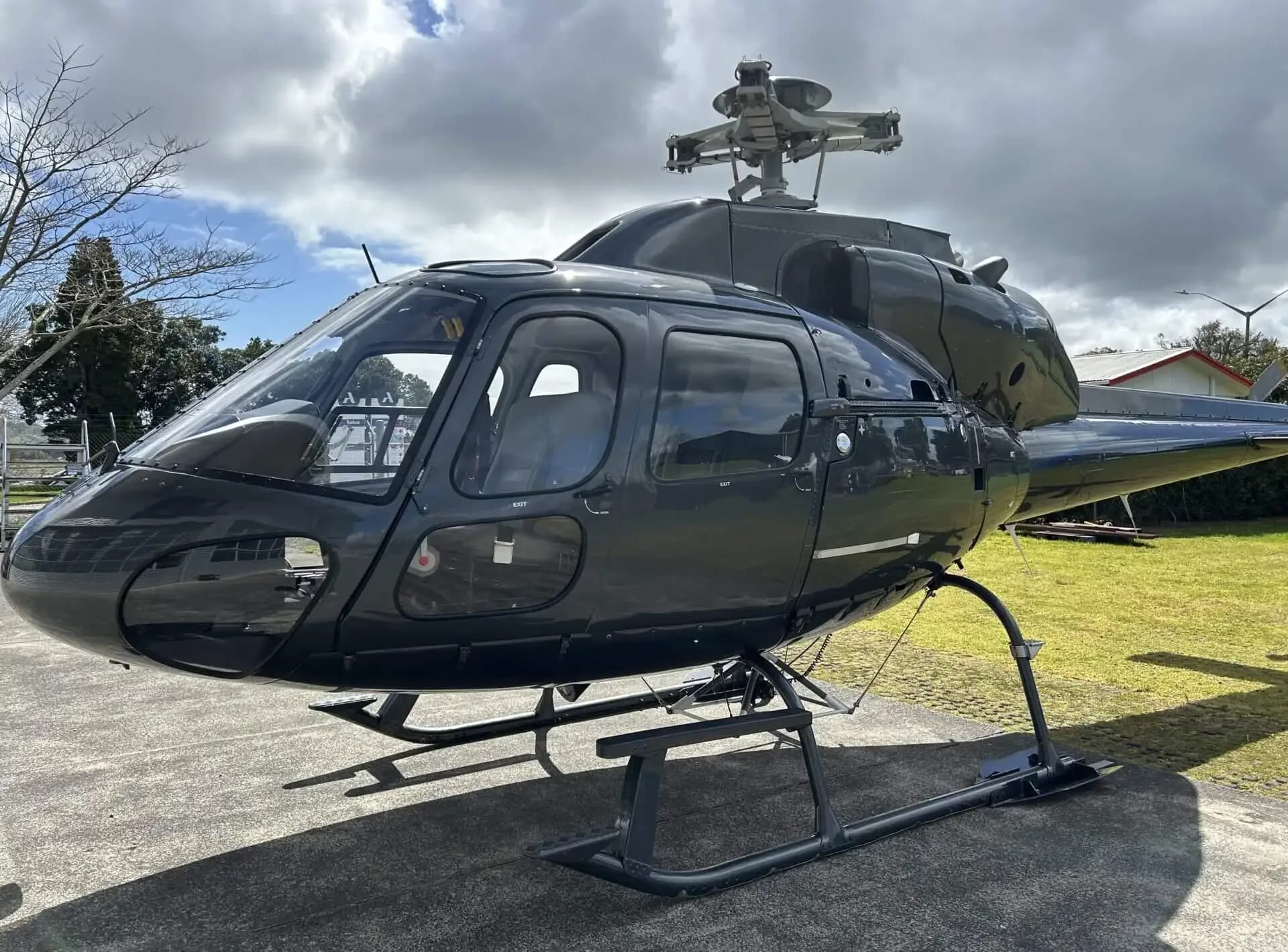 A dark grey Eurocopter AS355 F1 helicopter seen from the front-right, parked on a concrete pad with grass and trees in the background.