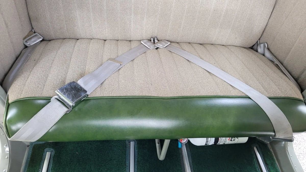 The rear bench seat of the Cessna 170 is upholstered in beige fabric with green trim.