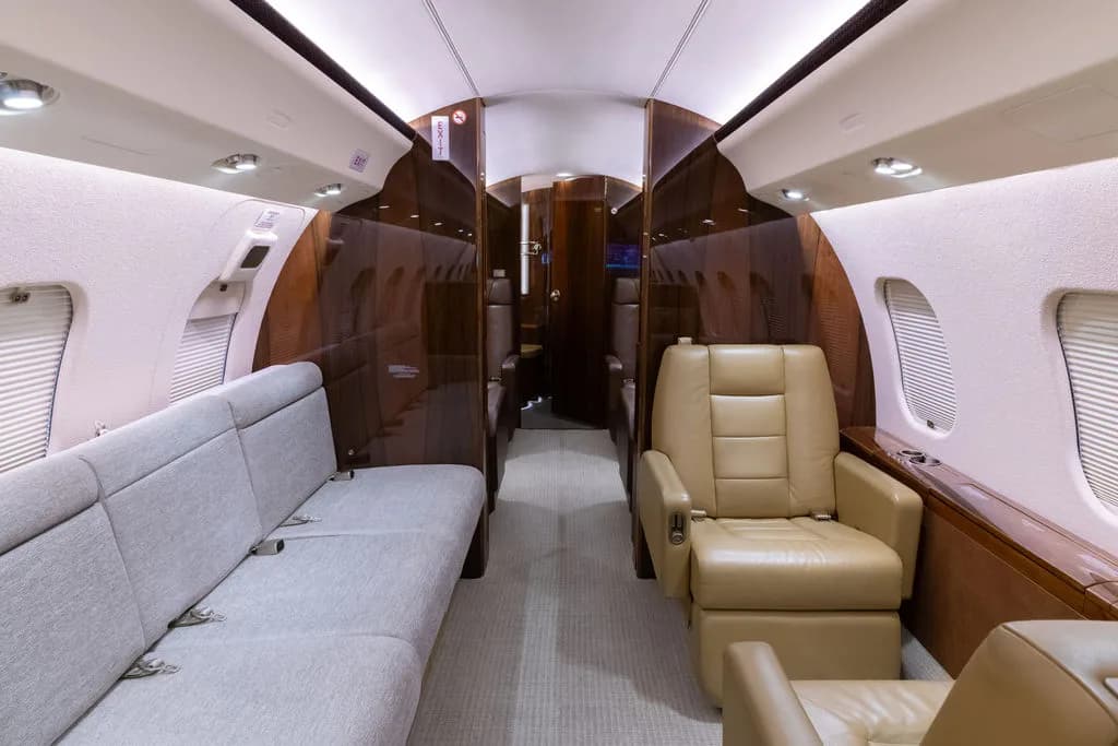 The aircraft's interior features a sofa, tan leather seats, and wood paneling.