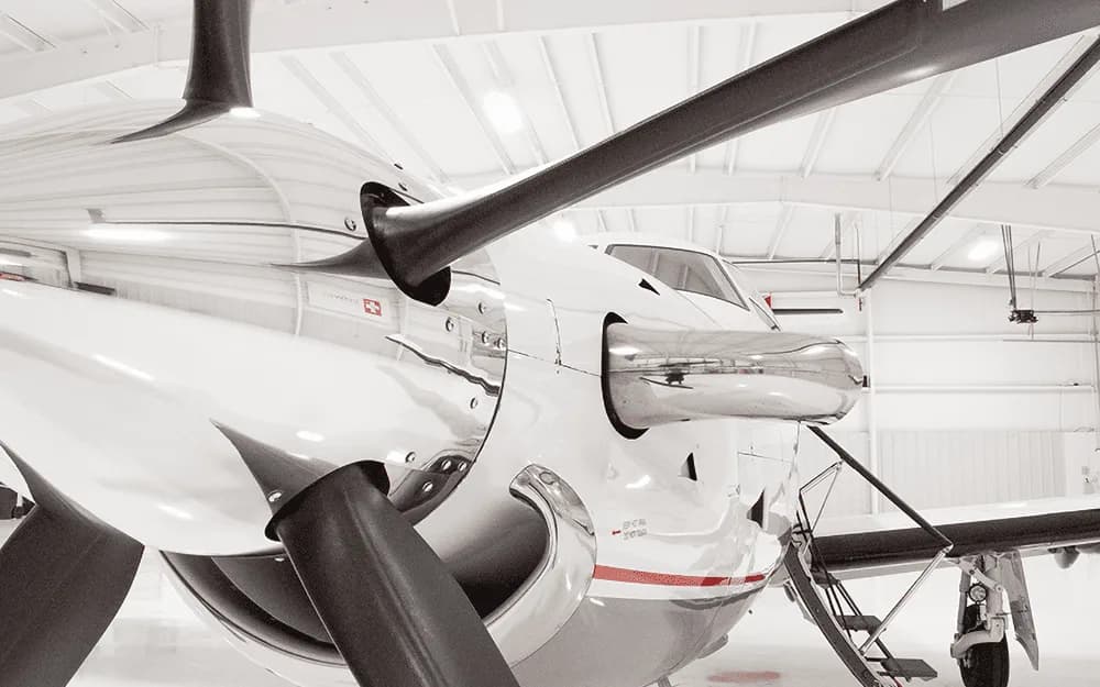 A close-up view of the propeller and nose of a white Pilatus PC-12 aircraft in a hangar.