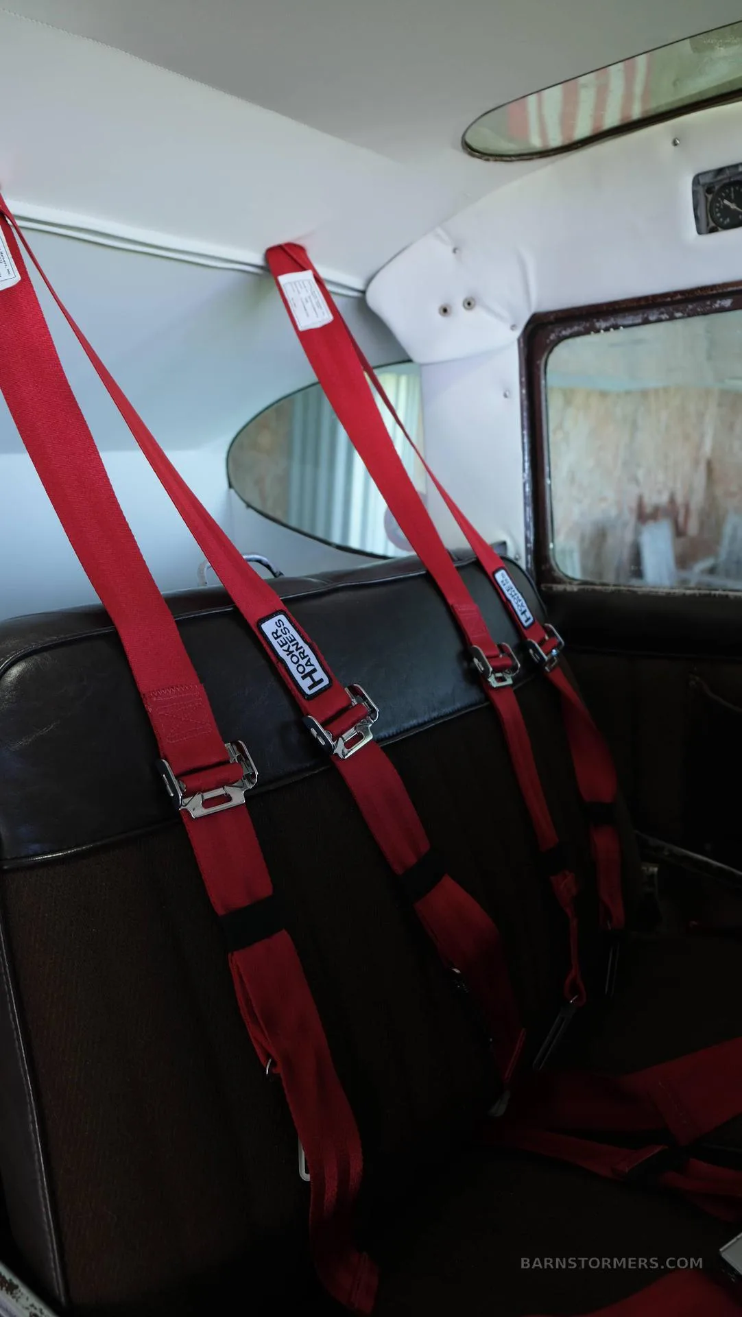The interior of a small aircraft cabin with brown seats and red Hooker Harness seatbelts.