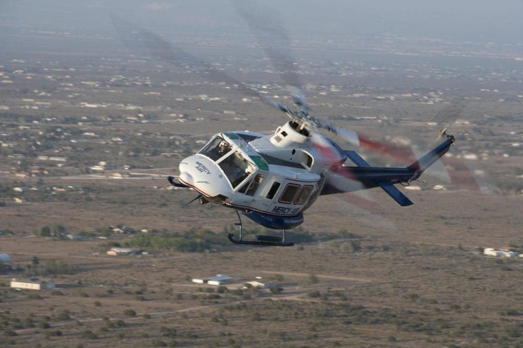 Mercy Air helicopter in flight over a desert landscape.