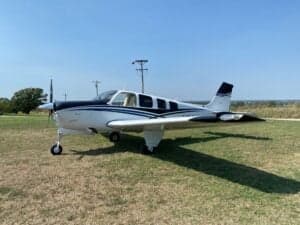 A Beechcraft Bonanza sits on a grassy field.