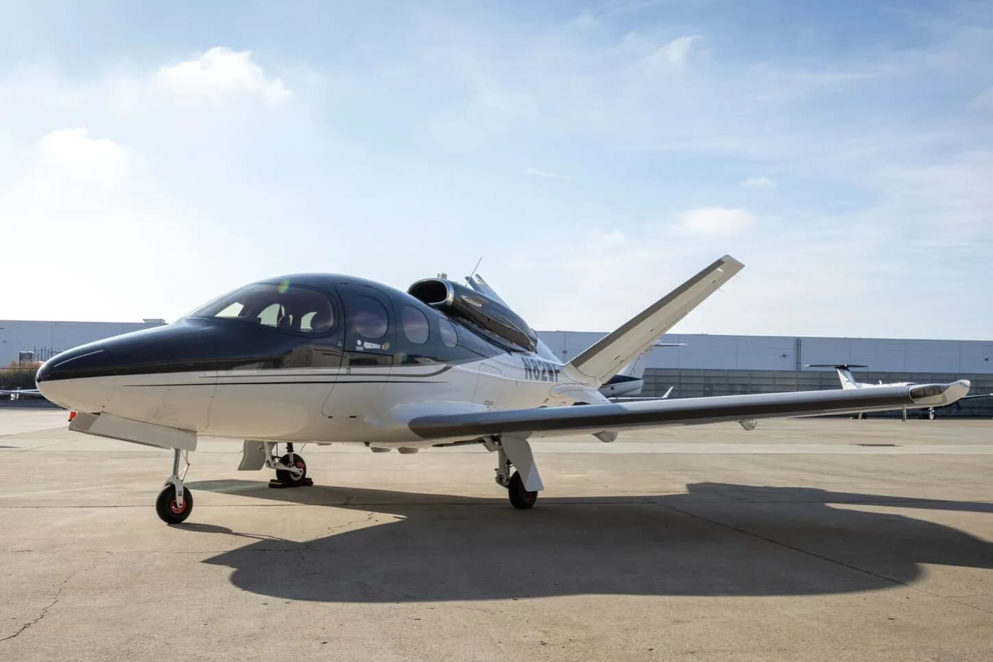 A side view of a white and dark grey Cirrus Vision Jet (N82WF) parked on an airport tarmac.