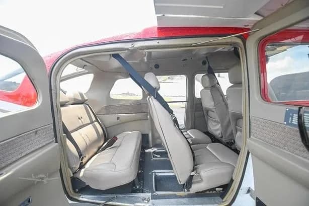 The light tan interior cabin of a small aircraft, showing two rows of seats with open doors.