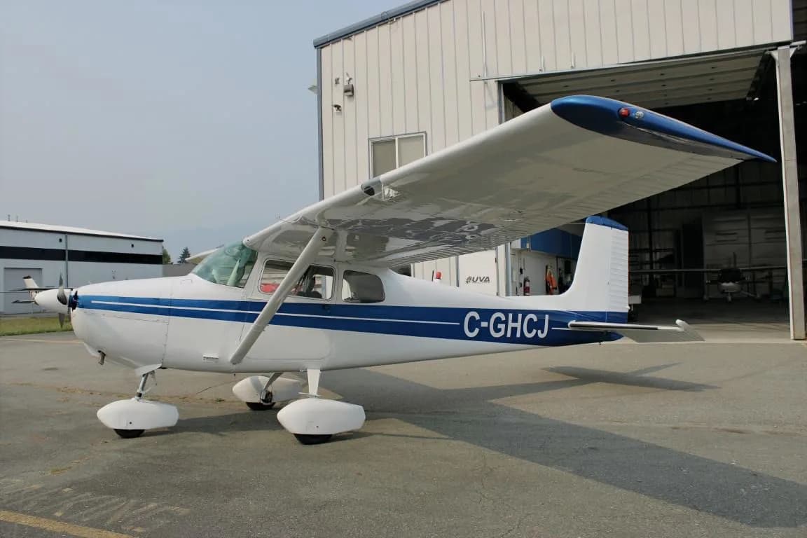 Cessna 172 with blue stripe parked in front of a hangar.